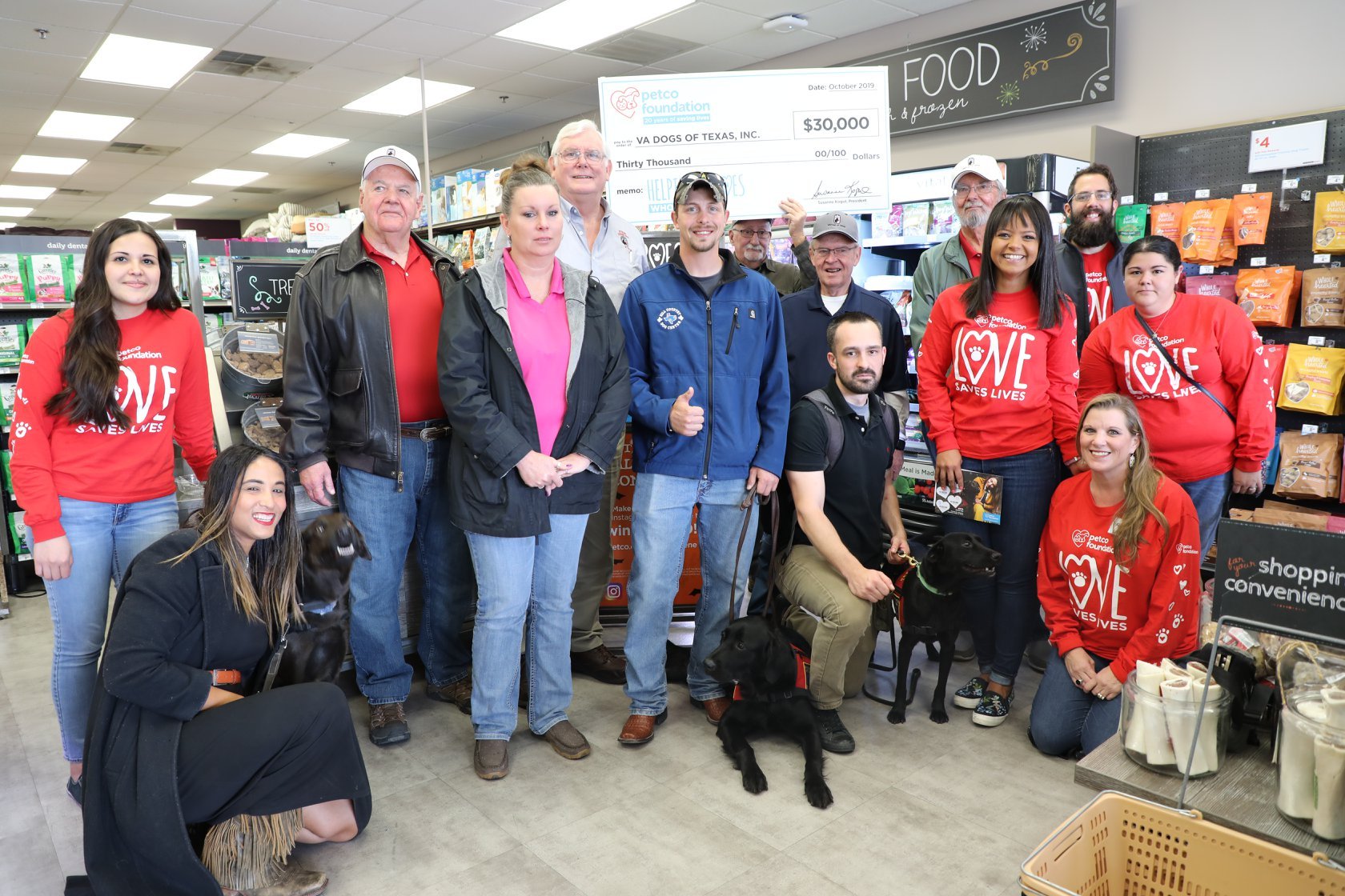 Group of people and dogs in a pet store, featuring a large check donation from Petco Foundation to VA Dogs of Texas, Inc.